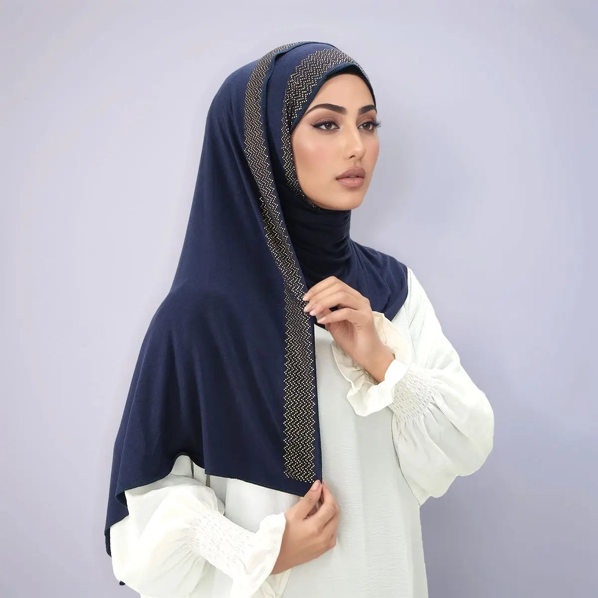 Eine Frau trägt einen dunkelblauen schimmernden Strass-Hijab und ein weißes Oberteil.
