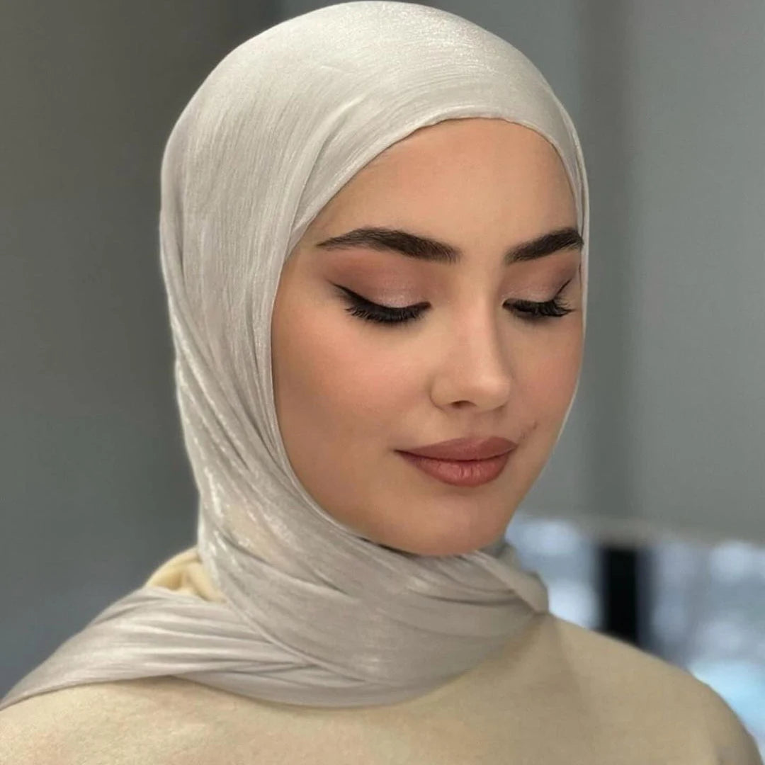 Une femme portant un hijab en mousseline crinkle argentée claire avec un maquillage doux et un haut de couleur crème.