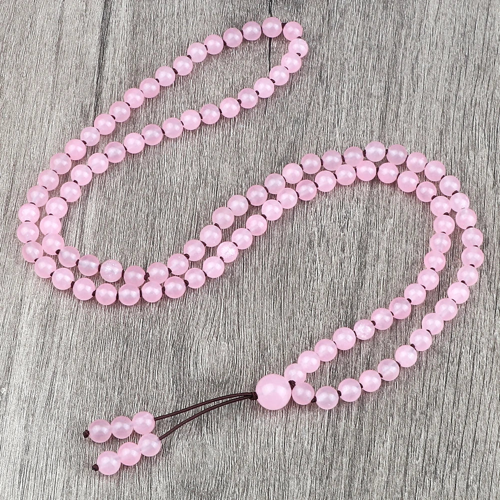 Eine Strang rosa Natursteinchen auf einer grauen Holzoberfläche.