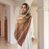A woman wearing a flowing beige watercolor print modal scarf draped over a white dress in an arched hallway.