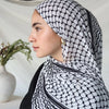 Una mujer vistiendo un elegante hiyab de gasa negra y blanca estampada cubriendo su cabeza y cuello.