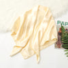 A pale yellow silk satin hijab scarf draped over a white fluffy surface.