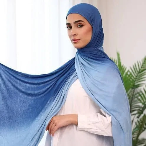 Una mujer vistiendo un pañuelo hijab de algodón degradado azul con una blusa blanca.