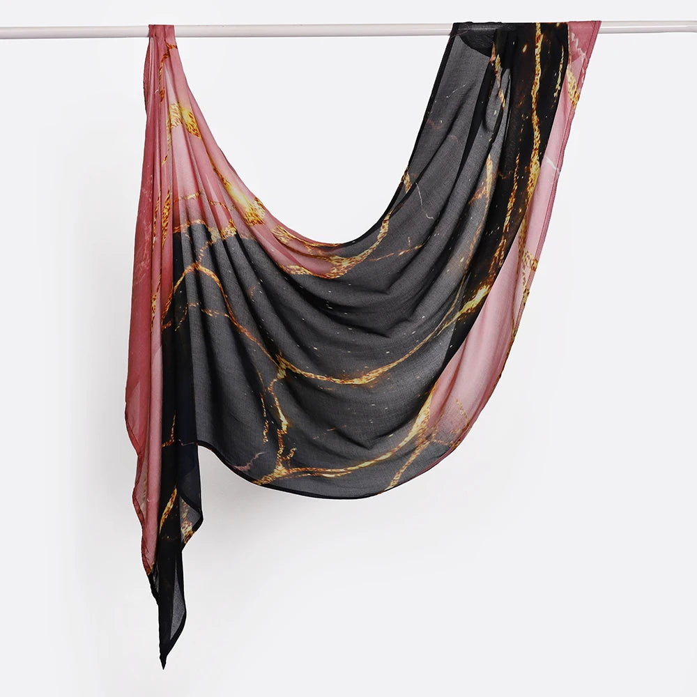 Voile de hijab imprimé noir et or drapé sur un cintre.