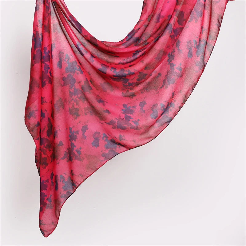 Ein leuchtend rosa und rotes Aquarellmuster-Schal mit Blumen, elegant drapiert.
