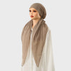 Une femme portant un foulard carré beige et un foulard assorti sur un haut blanc.