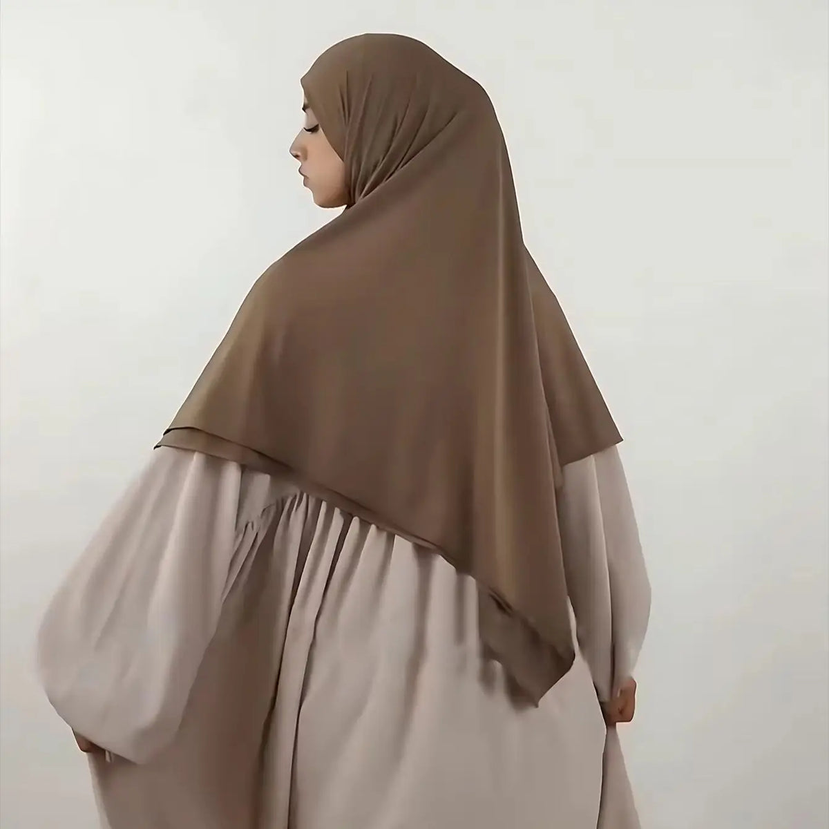 A woman wearing a beige hijab and flowing light-colored dress for Islamic wear.