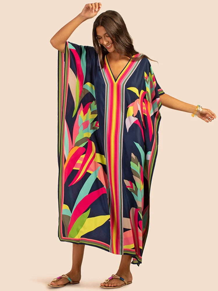 Una mujer modela un vestido caftán bohemio largo y fluido de playa estampado en azul oscuro con flores y rayas vibrantes