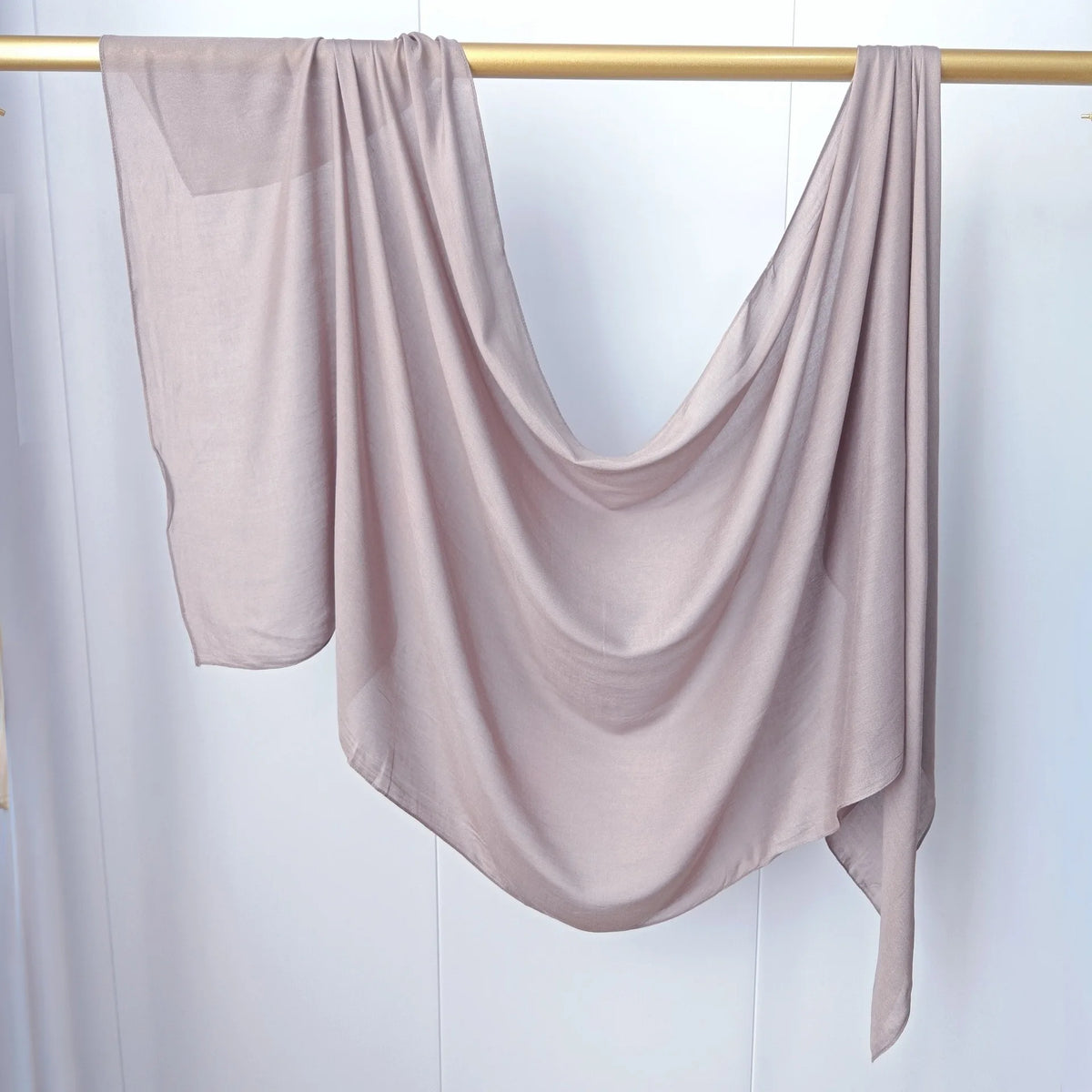 Un foulard modal de couleur beige clair drapé sur un cintre en bois.