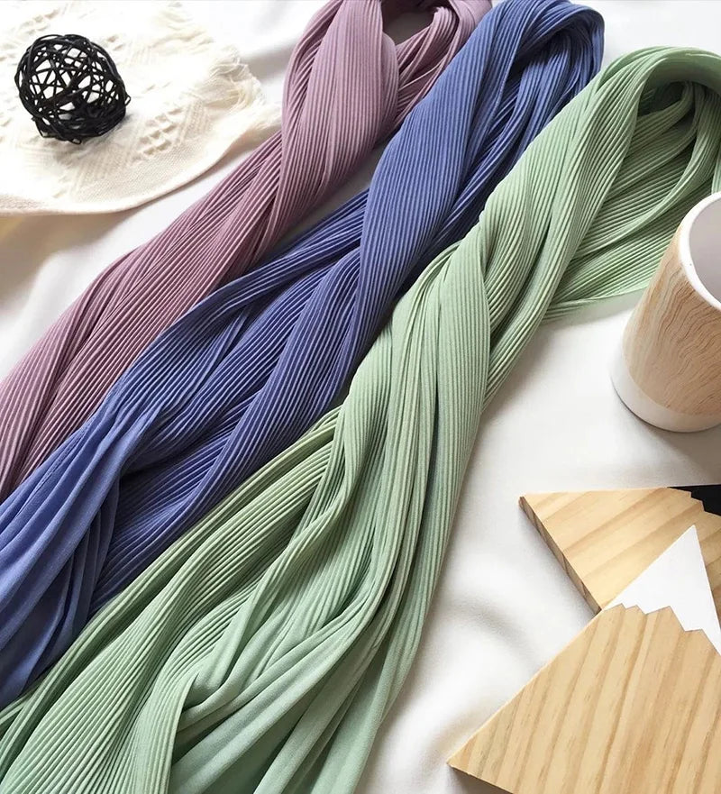 Eine Sammlung von Crinkle-Chiffon-Hijabs in Violett-, Blau- und Grüntönen auf einer weißen Oberfläche.