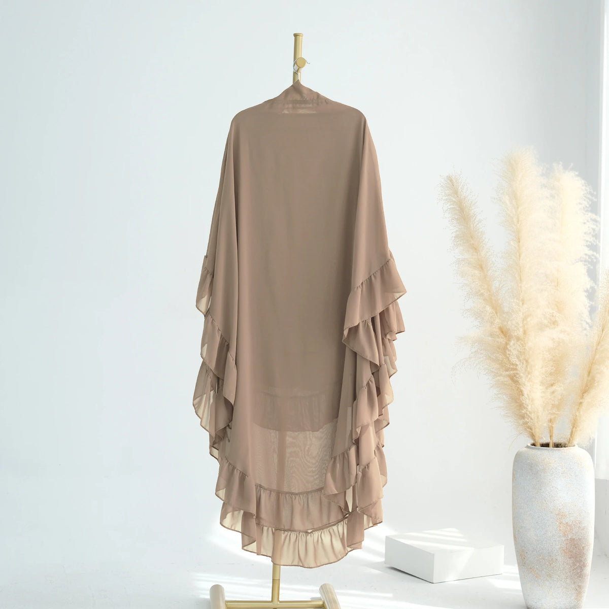 A sheer, beige ruffled two-layer chiffon hijab displayed on a gold hanger against a white background.