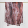 A sheer, printed linen hijab scarf in shades of dusty rose and brown is displayed hanging on a rod.