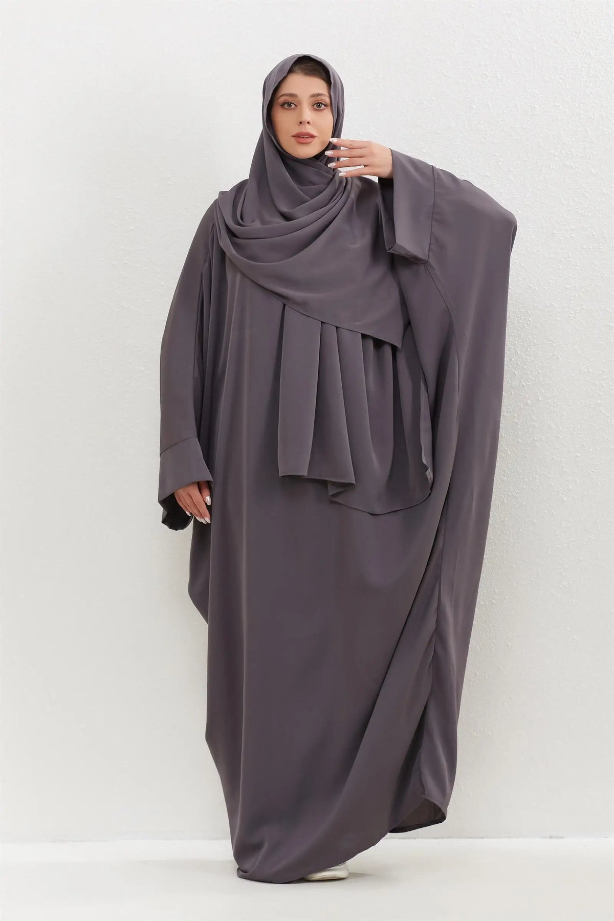 Eine Frau trägt ein traditionelles, schlichtes Abaya-Set in anthrazitgrauer Farbe mit passender Hijab.