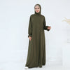 Una mujer vistiendo un vestido abaya suelto y vaporoso color verde oliva oscuro para la oración.