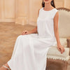 A woman wearing a white flowing modest abaya dress is seated on an antique chair.