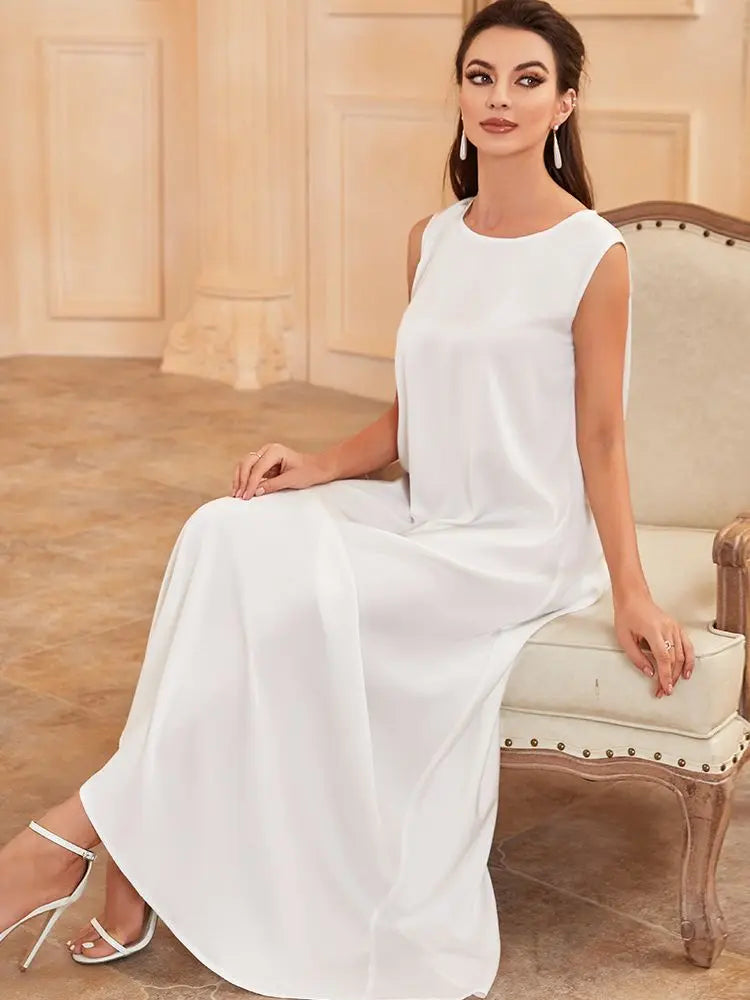 A woman wearing a white flowing modest abaya dress is seated on an antique chair.