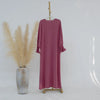 Un largo vestido abaya color rosa polvoriento colgado en una percha contra un fondo blanco.