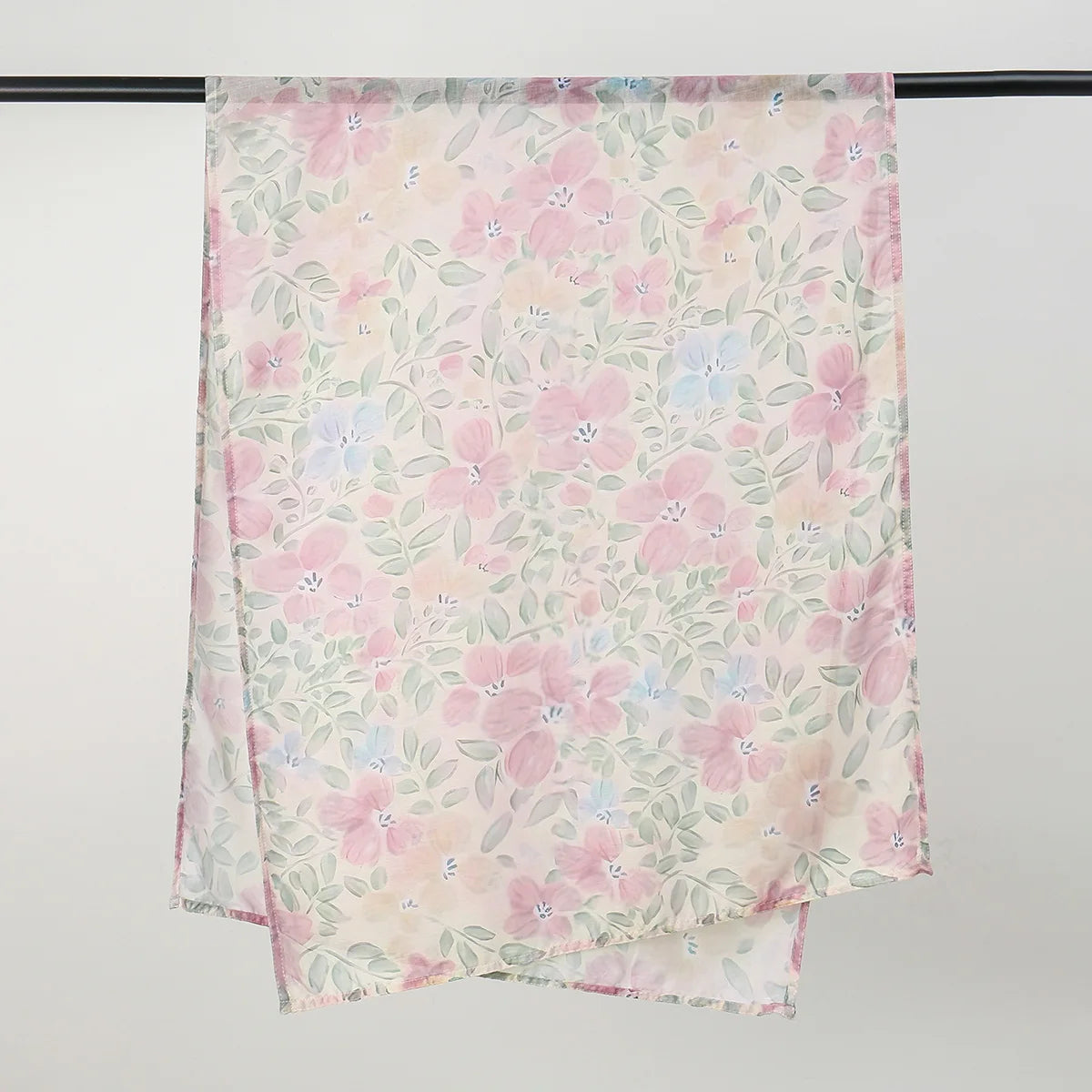 A light pink and green floral printed linen hijab scarf draped over a hanger.