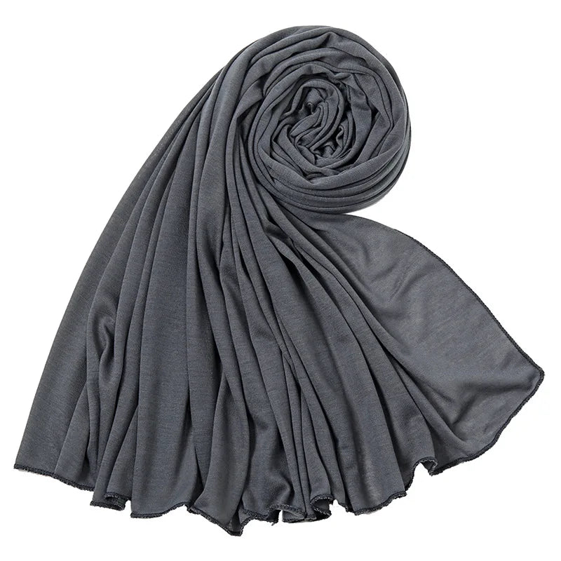 Un foulard hijab en jersey de coton gris foncé, roulé et drapé, montrant sa texture douce.