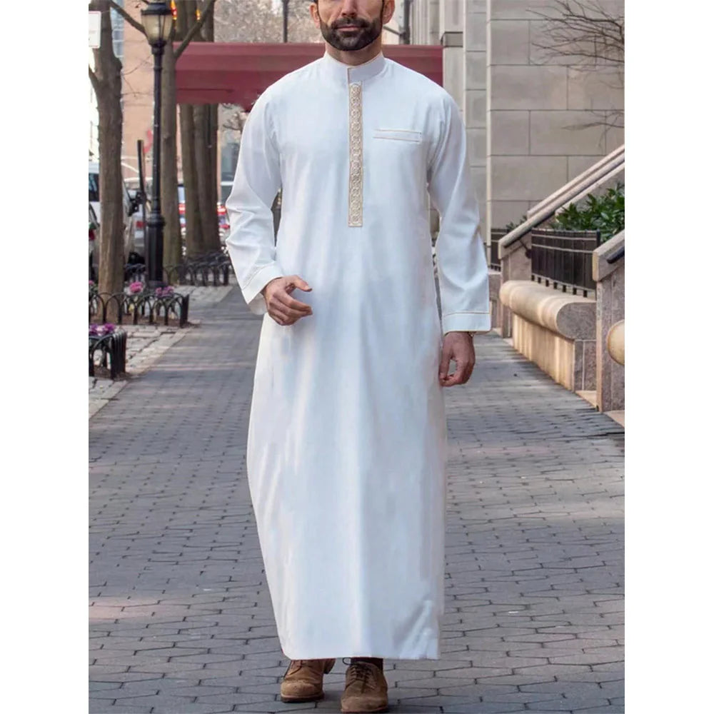 Un hombre vistiendo una jubba thobe islámica blanca tradicional con cuello mandarín y bordado dorado.