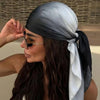 Une femme portant un foulard dégradé gris et noir noué autour de sa tête, regardant sur le côté.