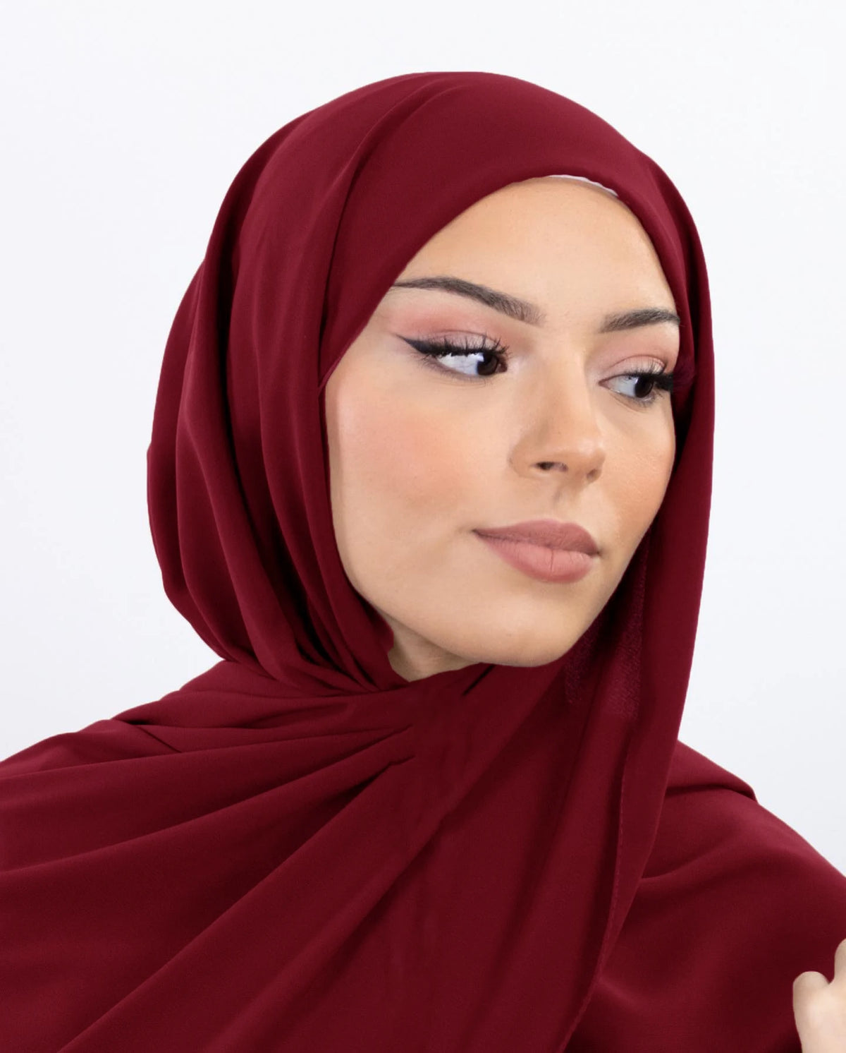 Une femme portant un hijab en mousseline marron foncé, regardant sur le côté.