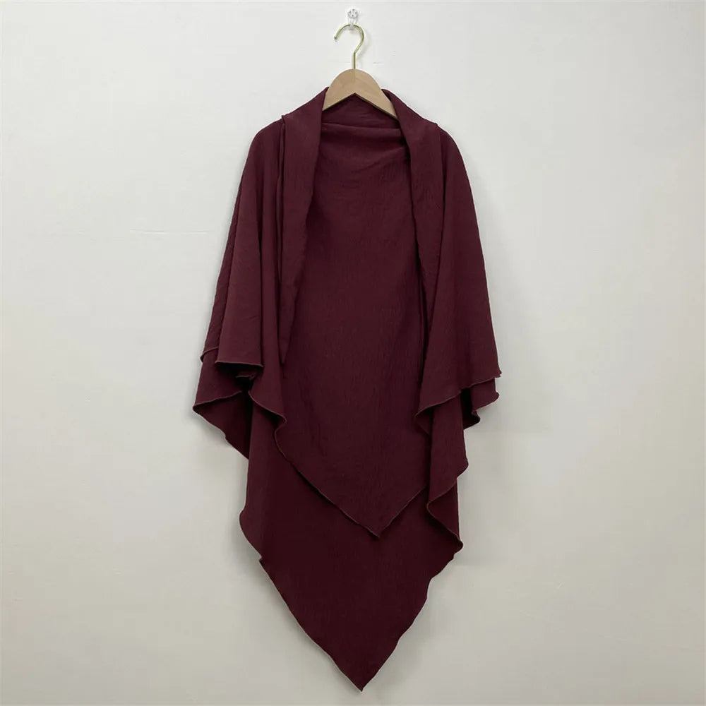 A deep burgundy two-layer everyday hijab scarf draped on a hanger against a white wall.