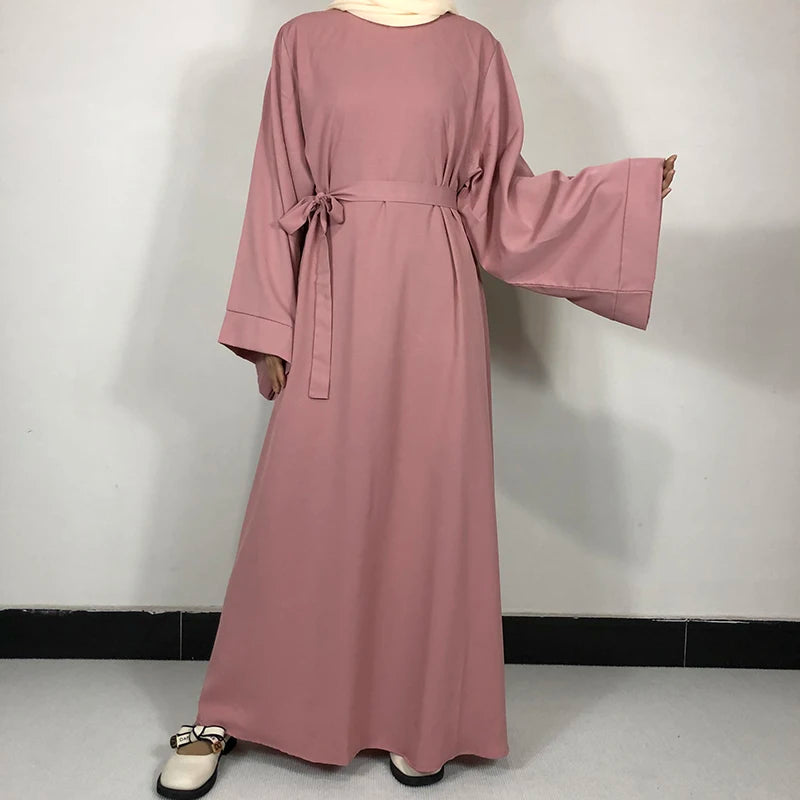 Une longue robe abaya rose poudré et poussiéreuse avec une ceinture, montrée sur un mannequin.