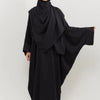 Eine Frau trägt ein schwarzes traditionelles, bedeckendes Abaya-Set mit passender Hijab.