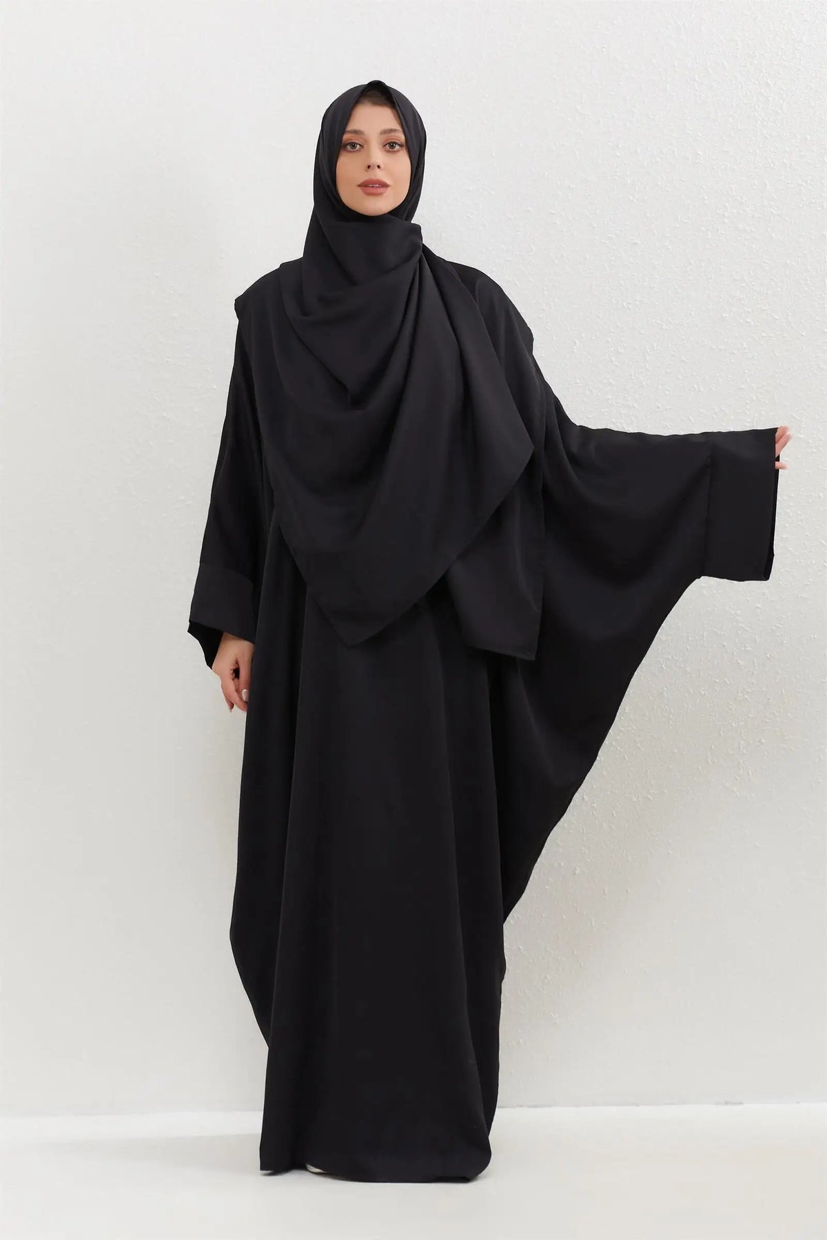 Eine Frau trägt ein schwarzes traditionelles, bedeckendes Abaya-Set mit passender Hijab.