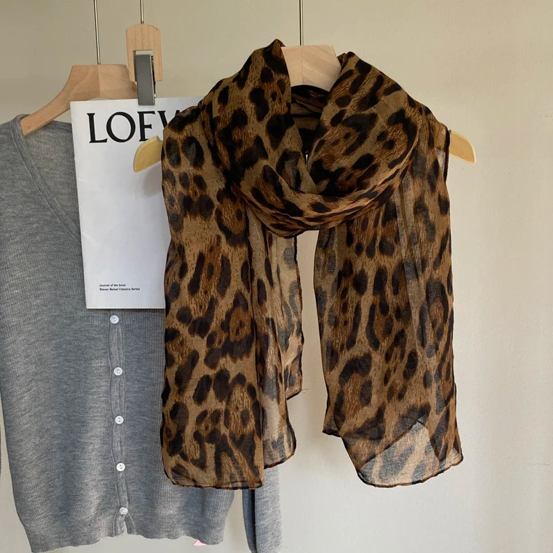 Écharpe pashmina à imprimé léopard marron drapée sur un cintre en bois sur fond clair.