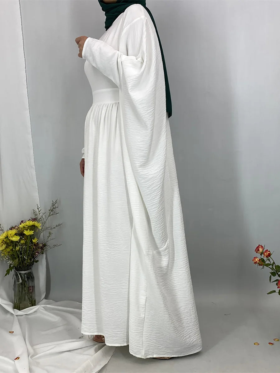 Eine Frau trägt eine elegante weiße Batwing-Abaya mit grüner Hijab in einem Studio.