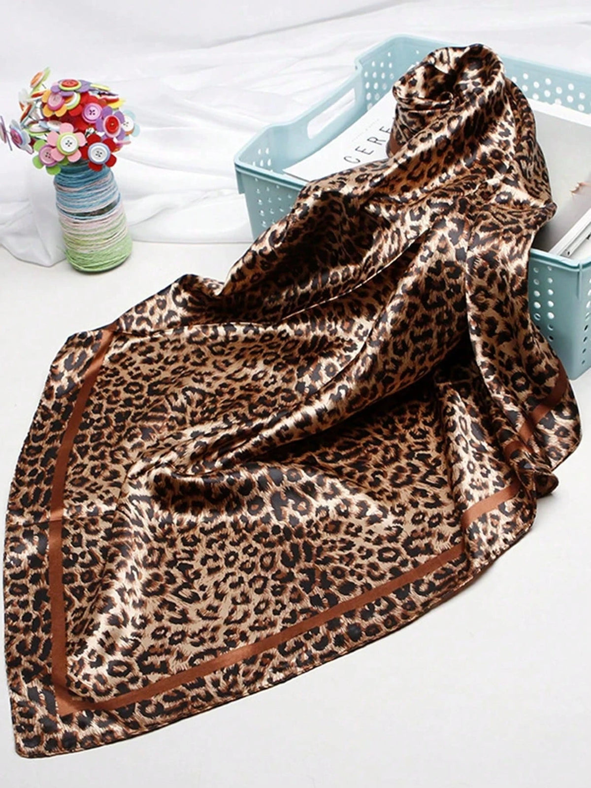 A luxurious brown leopard print silk satin scarf draped over a light blue tray.