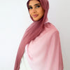 Une femme portant un foulard hijab rose dégradé et fluide sur un haut blanc.