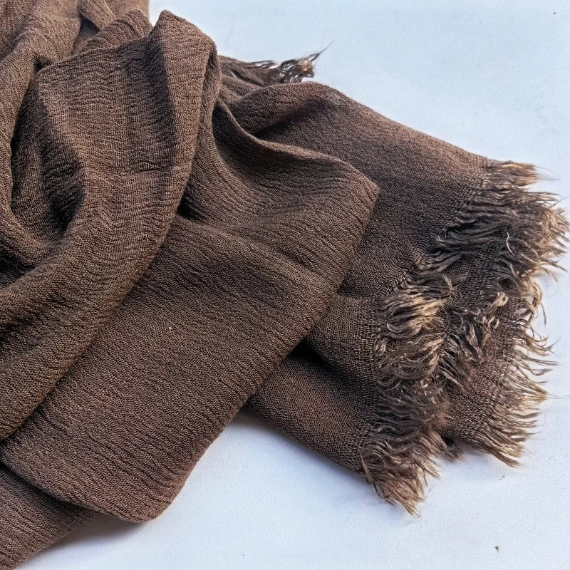 Gros plan d'un foulard hijab en coton viscose brun avec des pompons sur fond blanc.