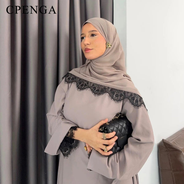 A woman wearing a beige lace abaya set with a matching hijab and holding a black quilted clutch.