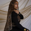 Una mujer vistiendo una blusa y falda negras con un pañuelo hijab de estampado de leopardo contra un fondo claro.