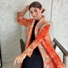 Eine Frau modelliert einen fließenden, plissierten Abaya-Cardigan in Orange und Rost über ein schwarzes Outfit.