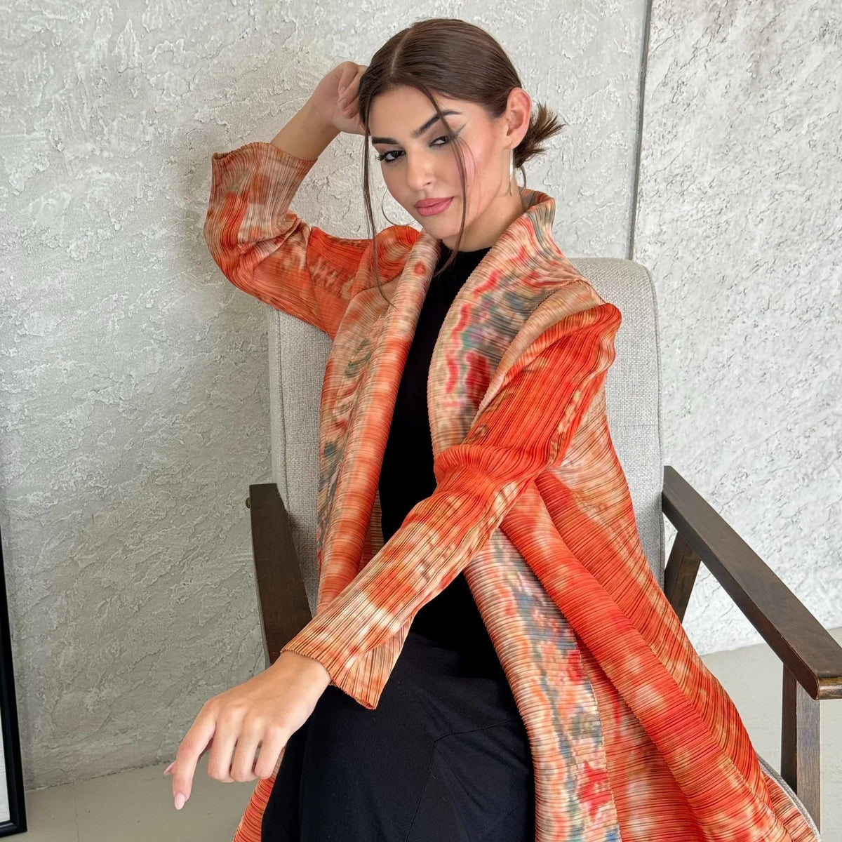Eine Frau modelliert einen fließenden, plissierten Abaya-Cardigan in Orange und Rost über ein schwarzes Outfit.