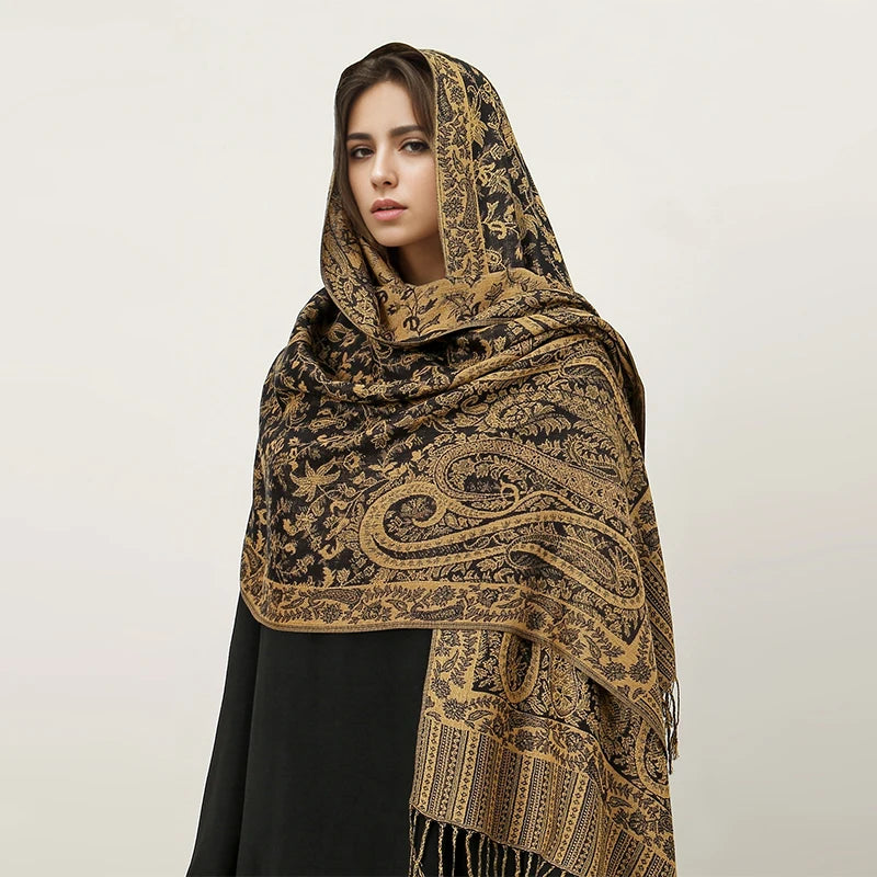 Una mujer modela un pañuelo pashmina de lujo con estampado paisley negro y dorado.