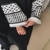 Gros plan sur une abaya noire avec broderie géométrique blanche sur les manches et le bas, portée par une personne.