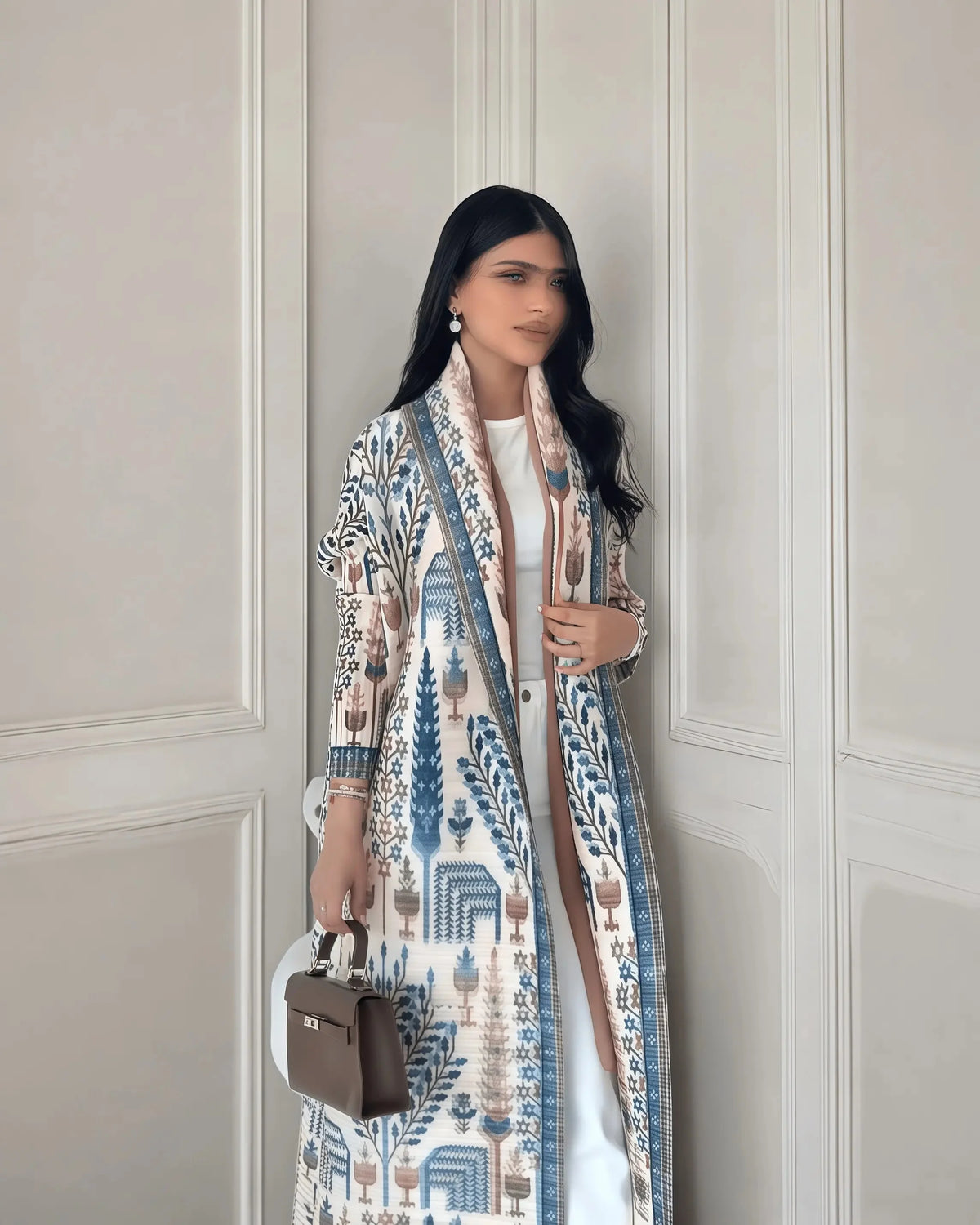 Una mujer vistiendo un cárdigan abaya plisado largo de color azul y beige estampado sobre una blusa blanca.