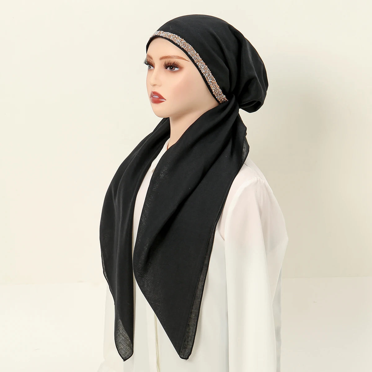 Una mujer modela un hijab negro con una diadema elástica de diamantes brillantes y ropa blanca.