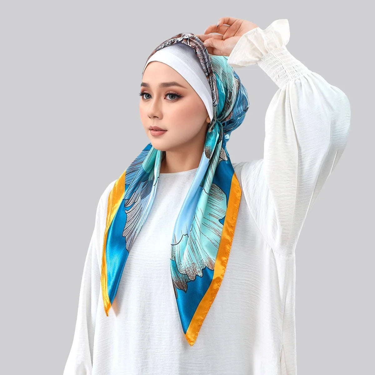Une femme portant un foulard instant bleu et or satiné avec une imprimation et du tissu blanc