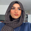 Eine Frau mit dunkelgrauem Polka-Dot-Jersey-Hijab und blauem Oberteil blickt in die Kamera.