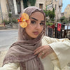 Une femme portant un foulard chiffon marron doux avec un bord en dentelle à cils, regardant directement l'appareil photo.