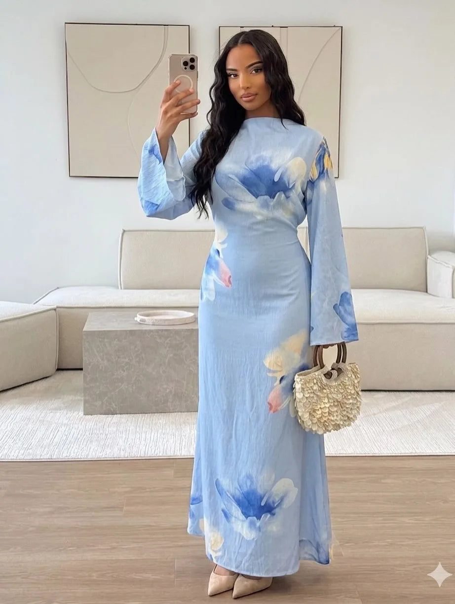 Eine Frau modelliert ein hellblaues Abaya-Kleid mit aquarelligen Blumenakzenten in einem hellen Innenraum.