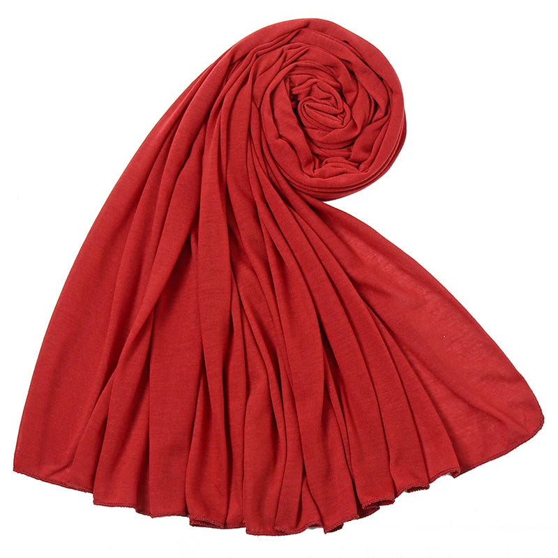 Ein leuchtend roschroter Baumwoll-Jersey-Hijab-Schal, gerollt und drapiert, zeigt seine weiche Textur.