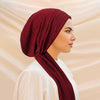 A woman wearing a deep maroon solid color turban hijab cap and white clothing, shown in profile.