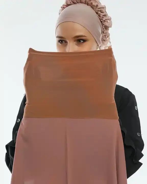 Une femme portant un hijab en mousseline beige et un haut marron, regardant l'appareil photo.